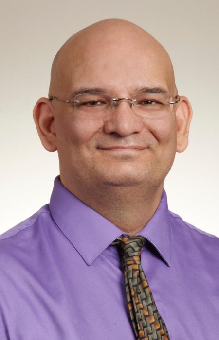 Headshot of William Deveau wearing glasses, a purple dress shirt, and tie